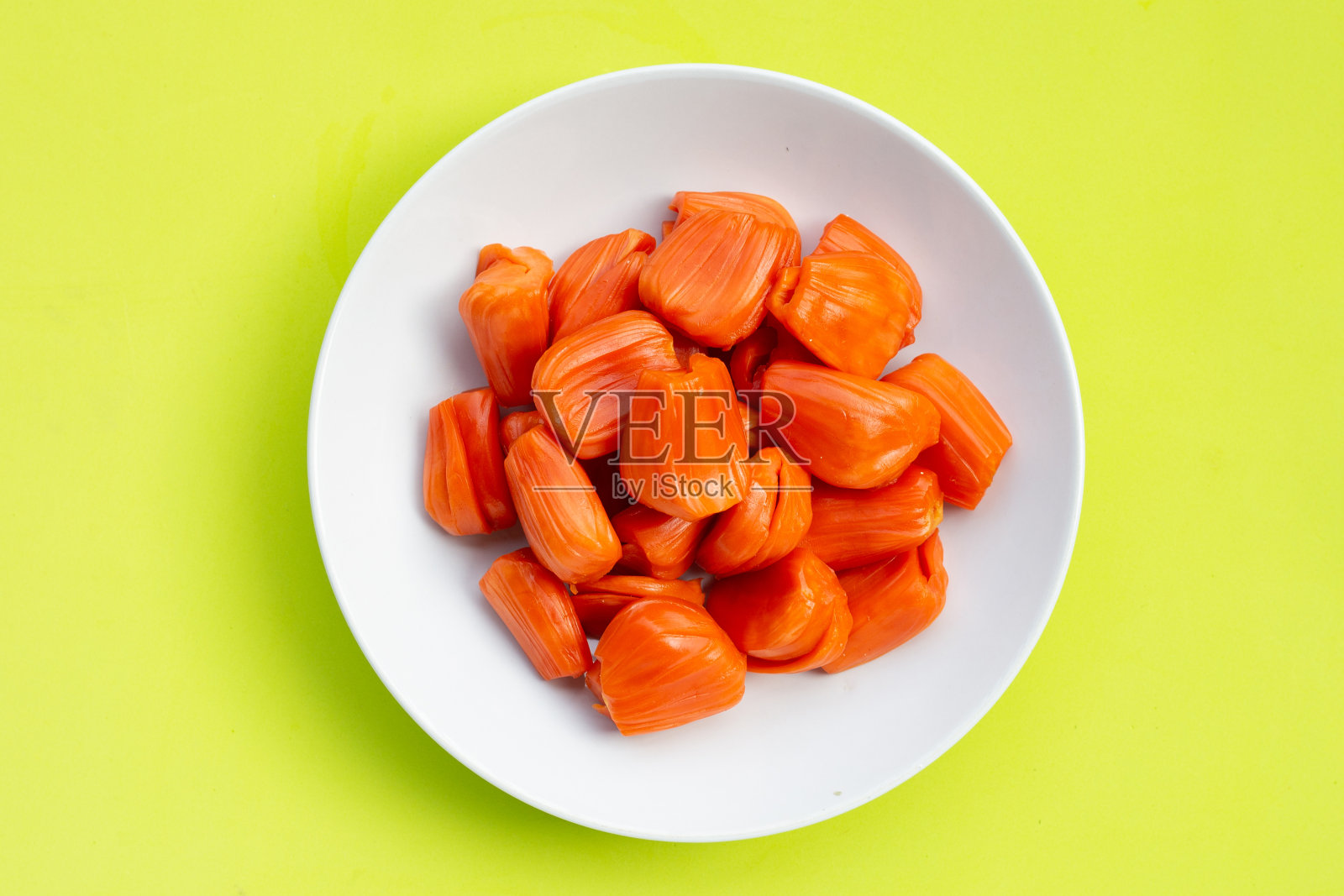 成熟的红色菠萝蜜在白色的盘子上，在绿色的背景。照片摄影图片