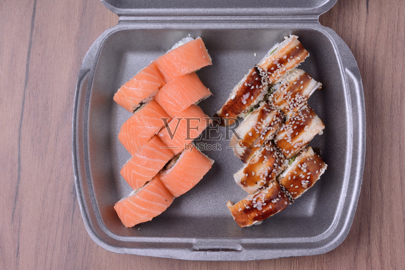 装在塑料容器里的鲑鱼和鳗鱼卷。木制背景，俯视图照片摄影图片