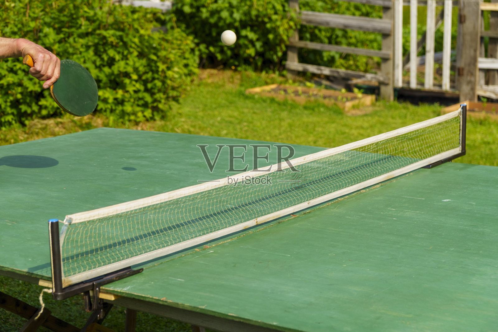 手拿球拍，在户外的院子里打乒乓球，击球照片摄影图片