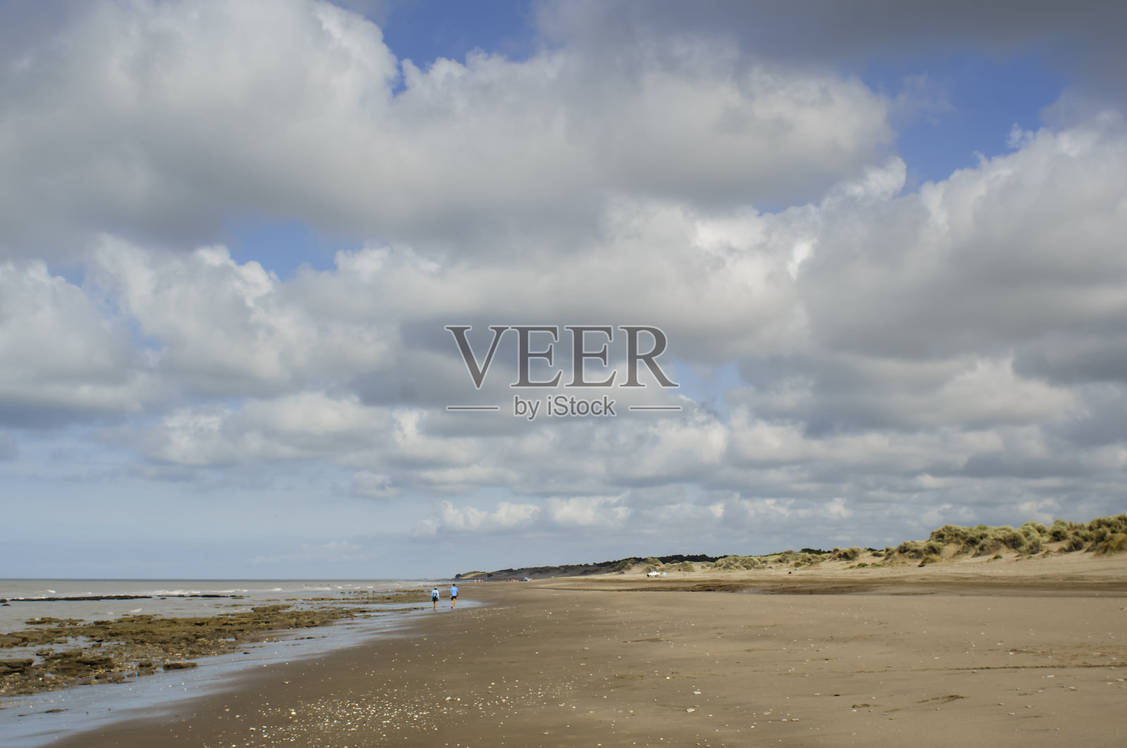 沙滩上有人在散步，广阔的蓝天上飘着白云照片摄影图片