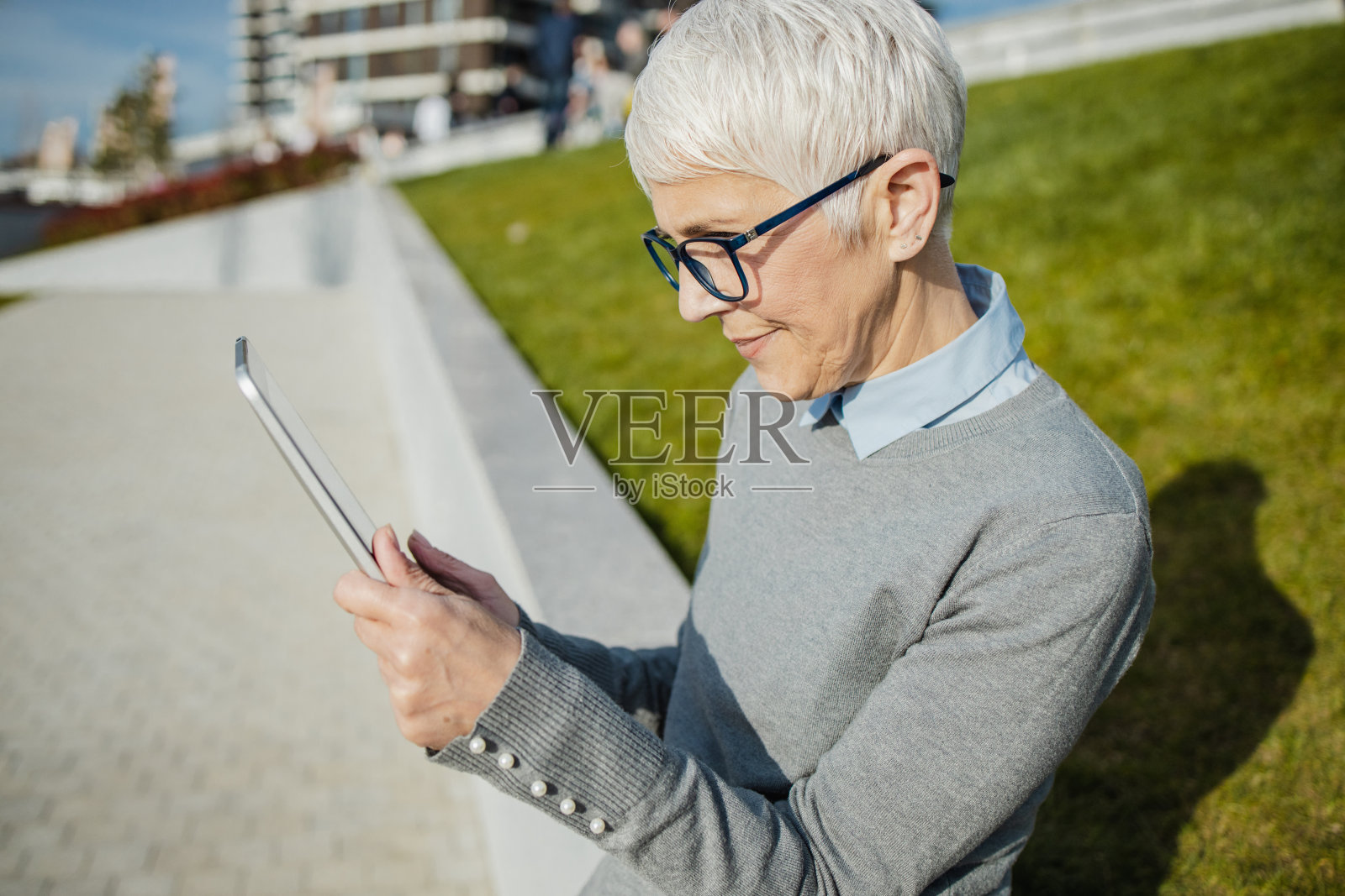 一位在阳光明媚的日子里拿着平板电脑的高级女士的肖像照片摄影图片