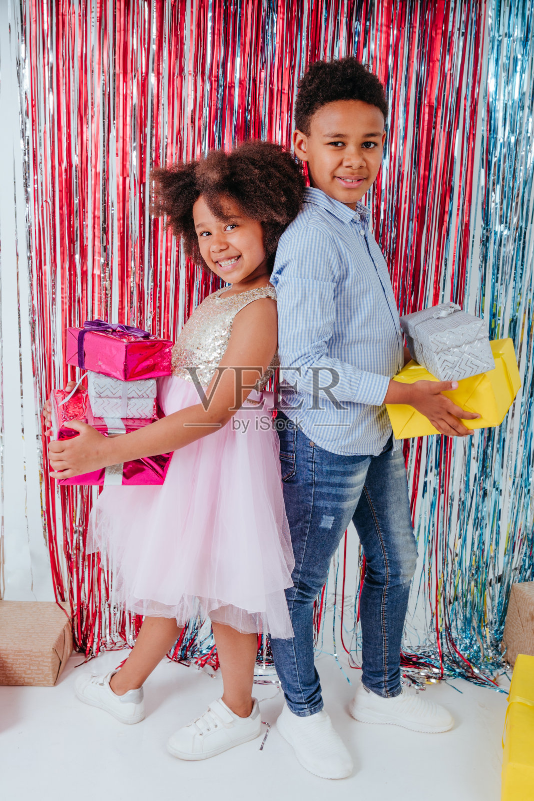 快乐的女孩和男孩站在铝箔窗帘旁边，拿着礼物盒照片摄影图片