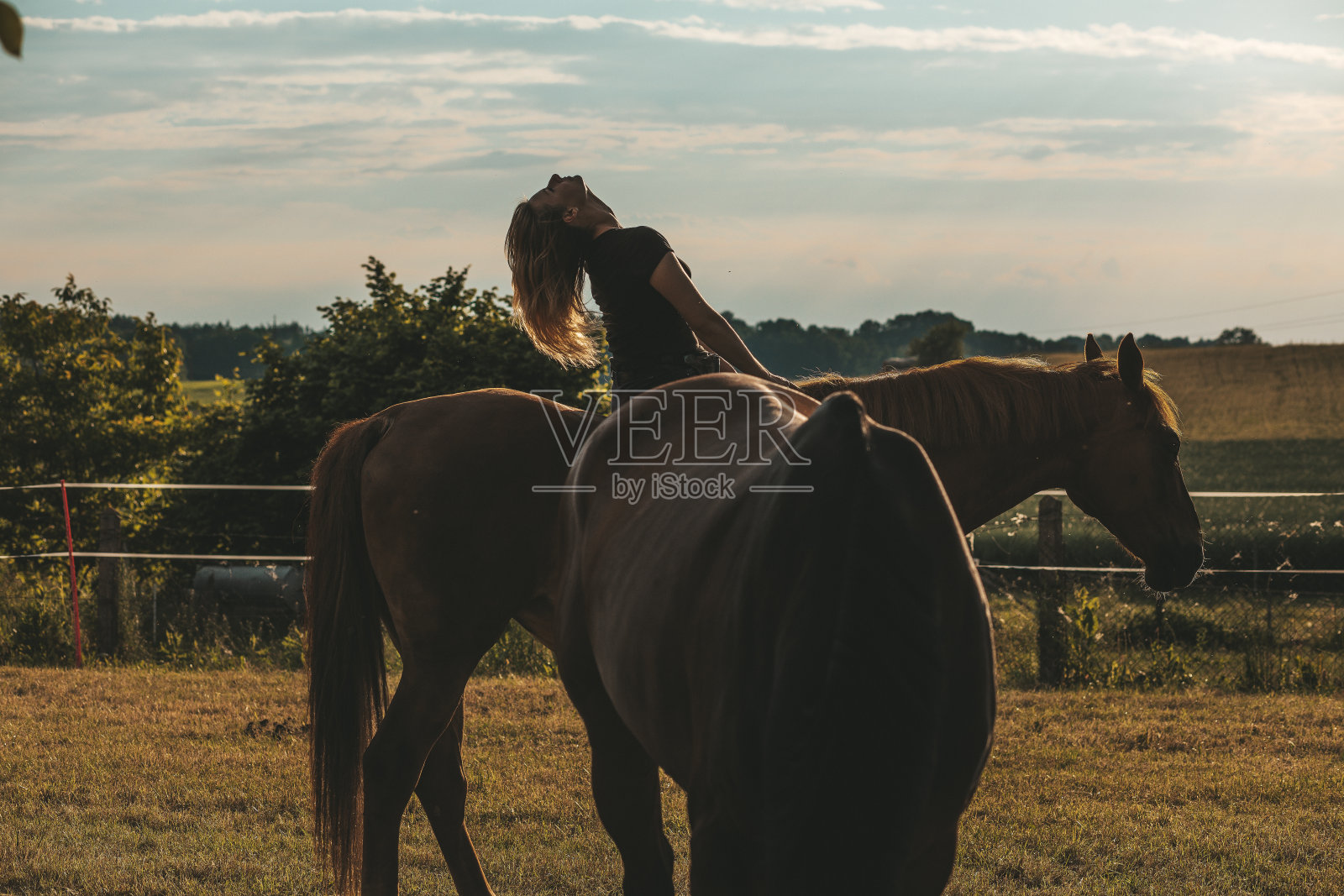 年轻的女主人笑了，她坐在她的马对夕阳的天空。美丽和健康。享受生活。这是伟大的时间。照片摄影图片