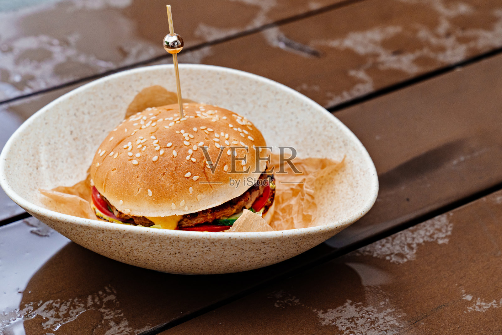 湿漉漉的木桌上，盘子里装着肉饼和蔬菜的汉堡。照片摄影图片