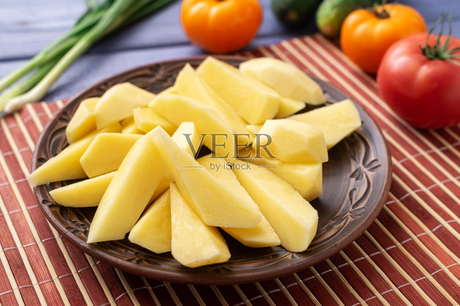 去皮切好的生土豆块茎和蔬菜放在厨房桌子上的盘子里。准备做饭。照片摄影图片