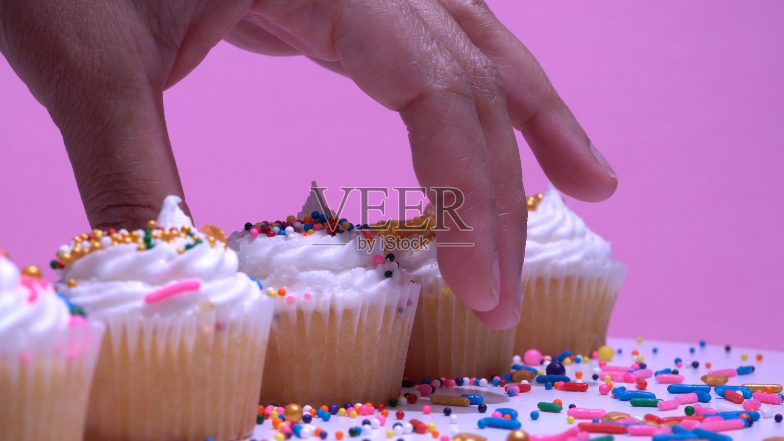 女人的手挑选装饰纸杯蛋糕。浅景深的焦点。近距离看松饼。粉红色的背景。在周年或生日时提供甜点。照片摄影图片
