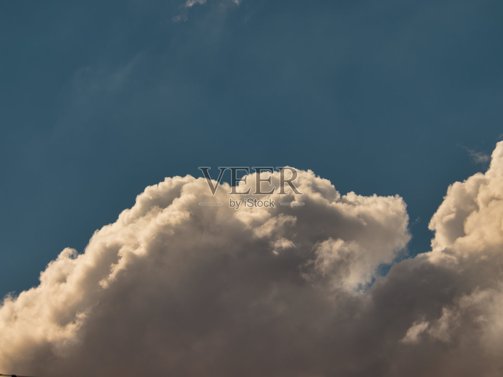 一大片蓬松的白色积云的顶部，一些灰色的影子漂浮在蓝天的地平线上。照片摄影图片