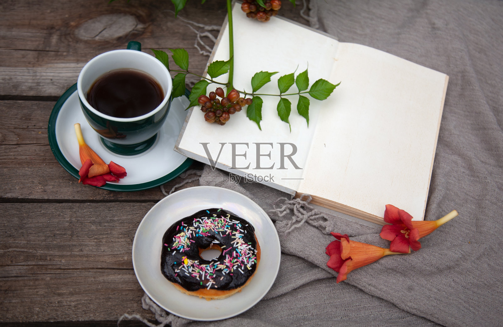 一杯咖啡(茶)，一个盘子里的甜甜圈，一个笔记本(打开的书)和一束花在一张木桌上照片摄影图片