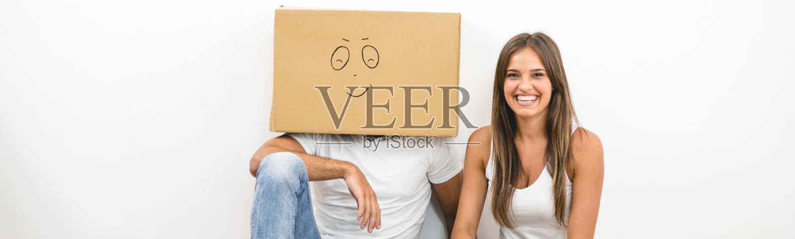 头上顶着一个纸箱的男人坐在一个女人旁边照片摄影图片