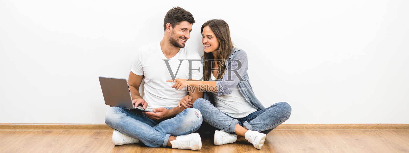 一个快乐的男人和一个带着笔记本电脑的女人坐在空墙旁边照片摄影图片