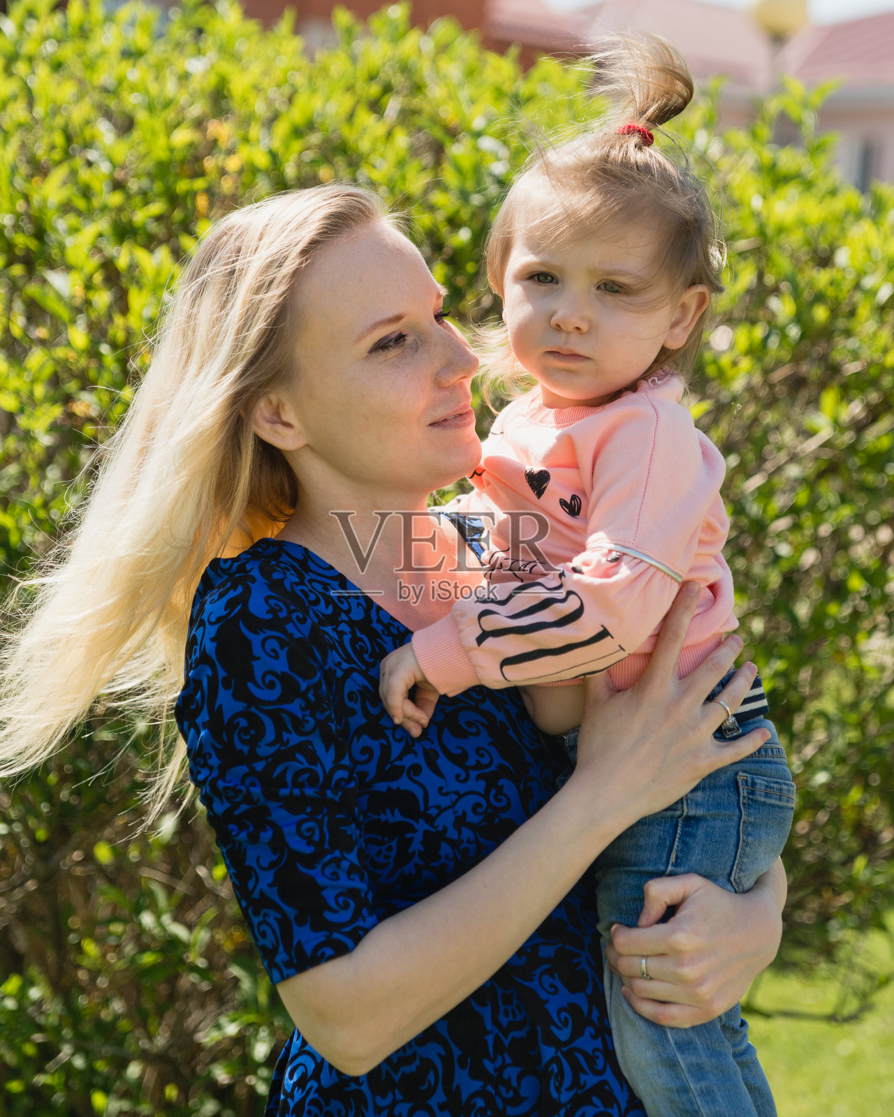 一位年轻美丽的母亲看着蹒跚学步的女儿。怀里抱着一个女孩。一个阳光明媚的一天。幸福照片摄影图片
