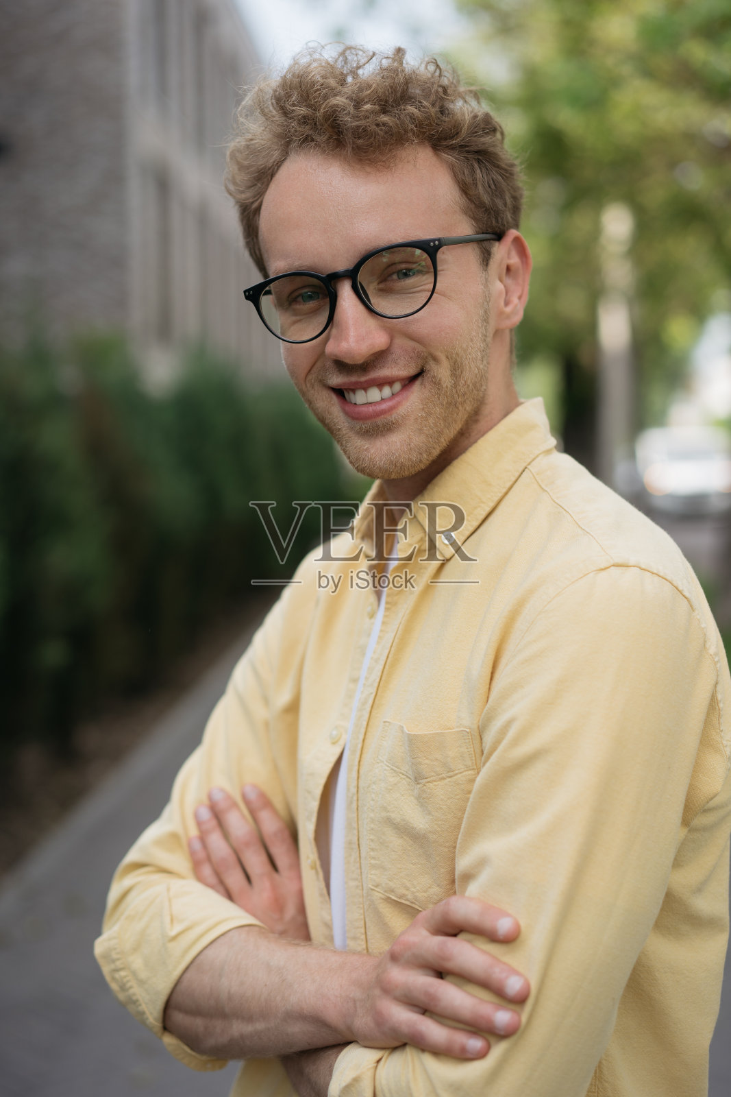 英俊的微笑男子穿着黄色衬衫和时尚的眼镜看着摄像机站在街上。成功的商业和职业理念照片摄影图片