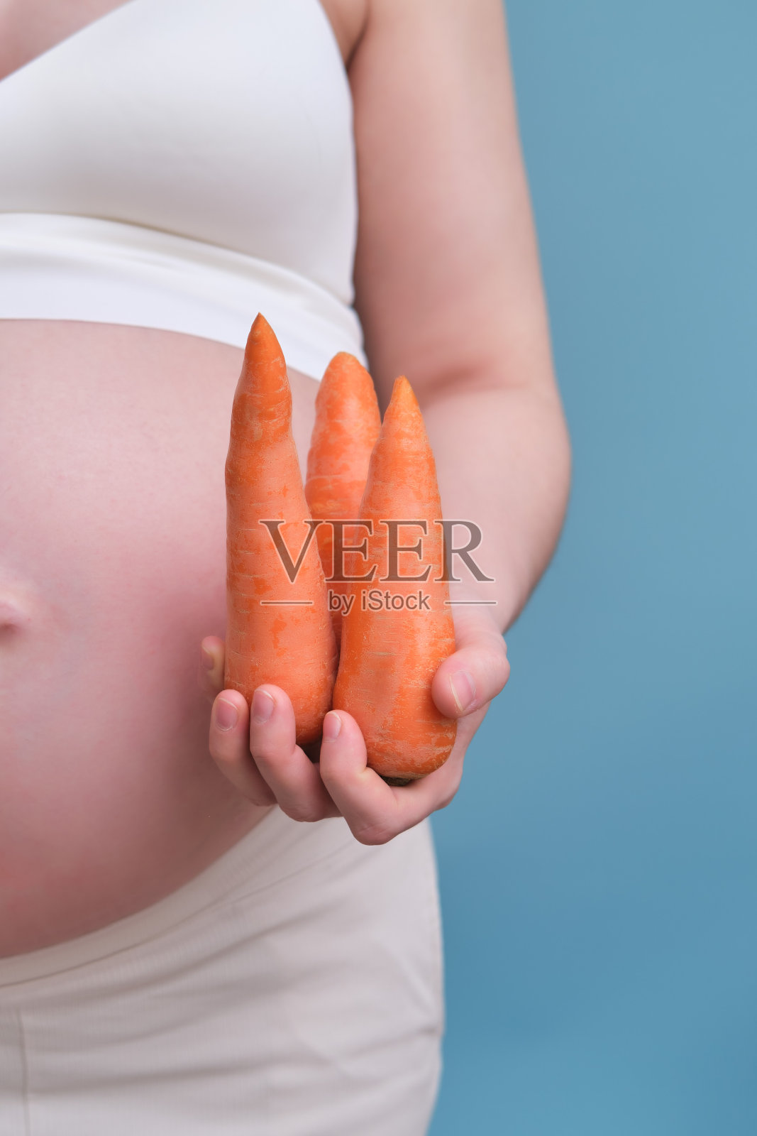 孕妇手里拿着三根胡萝卜，蓝色背景照片摄影图片