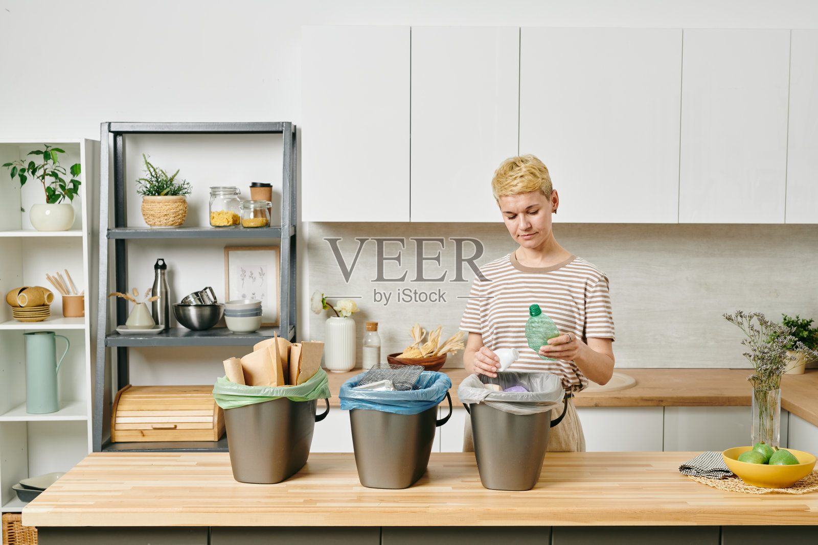 年轻的金发女人把垃圾分成三个箱子照片摄影图片