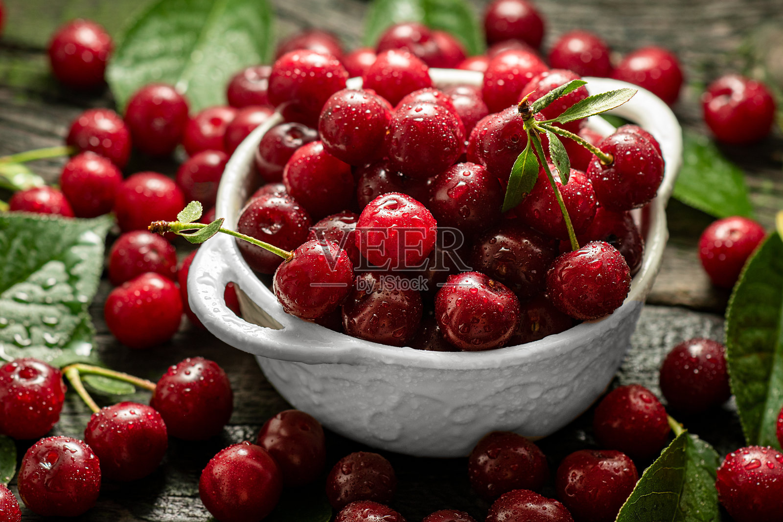 新鲜的甜樱桃碗与树叶在木制桌子上。水滴在新鲜的酸樱桃浆果上照片摄影图片