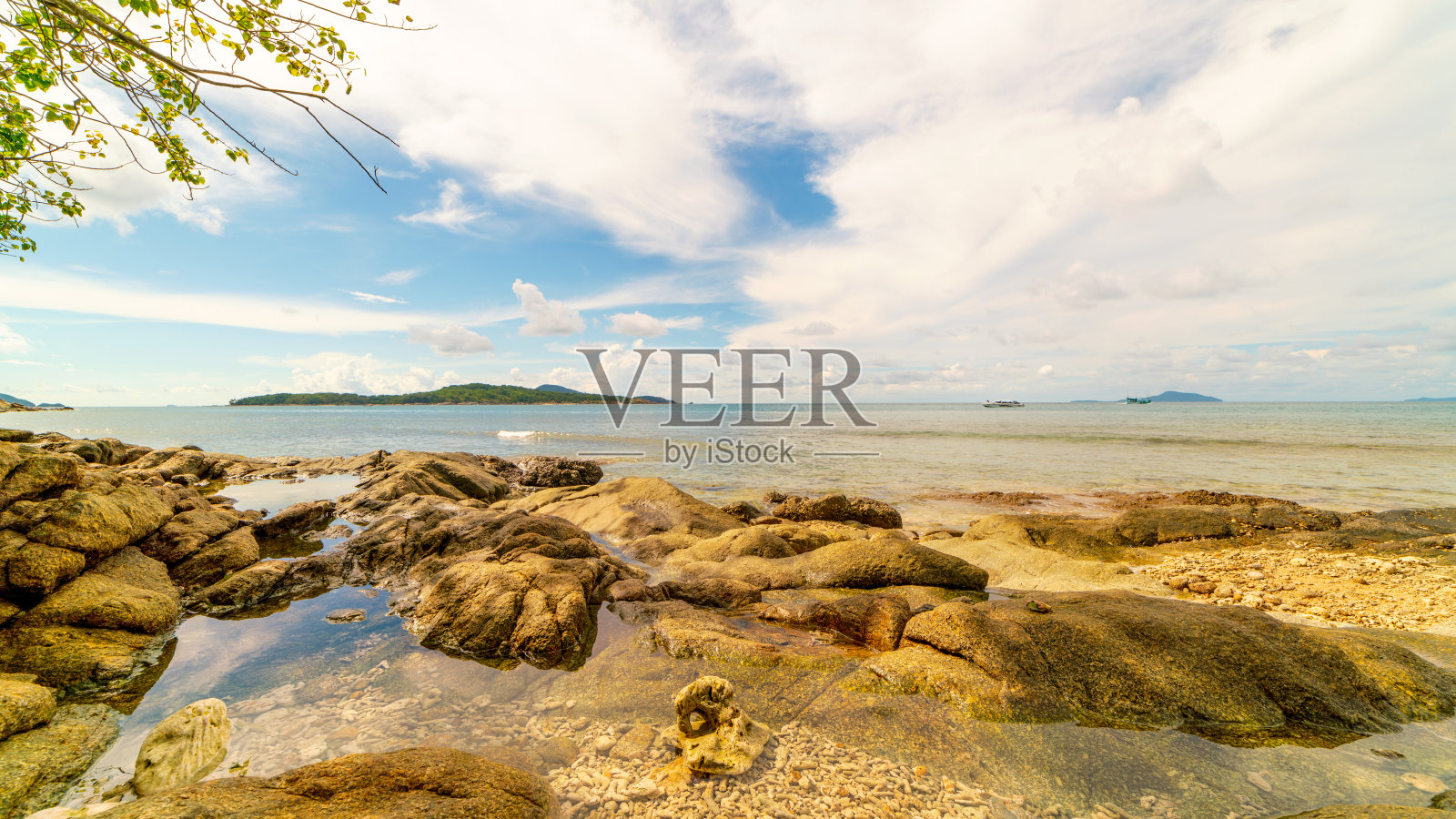 岩石海岸在晴朗的蓝天下，在早晨和树叶树框架背景美丽的大海和小岛在泰国普吉岛。照片摄影图片