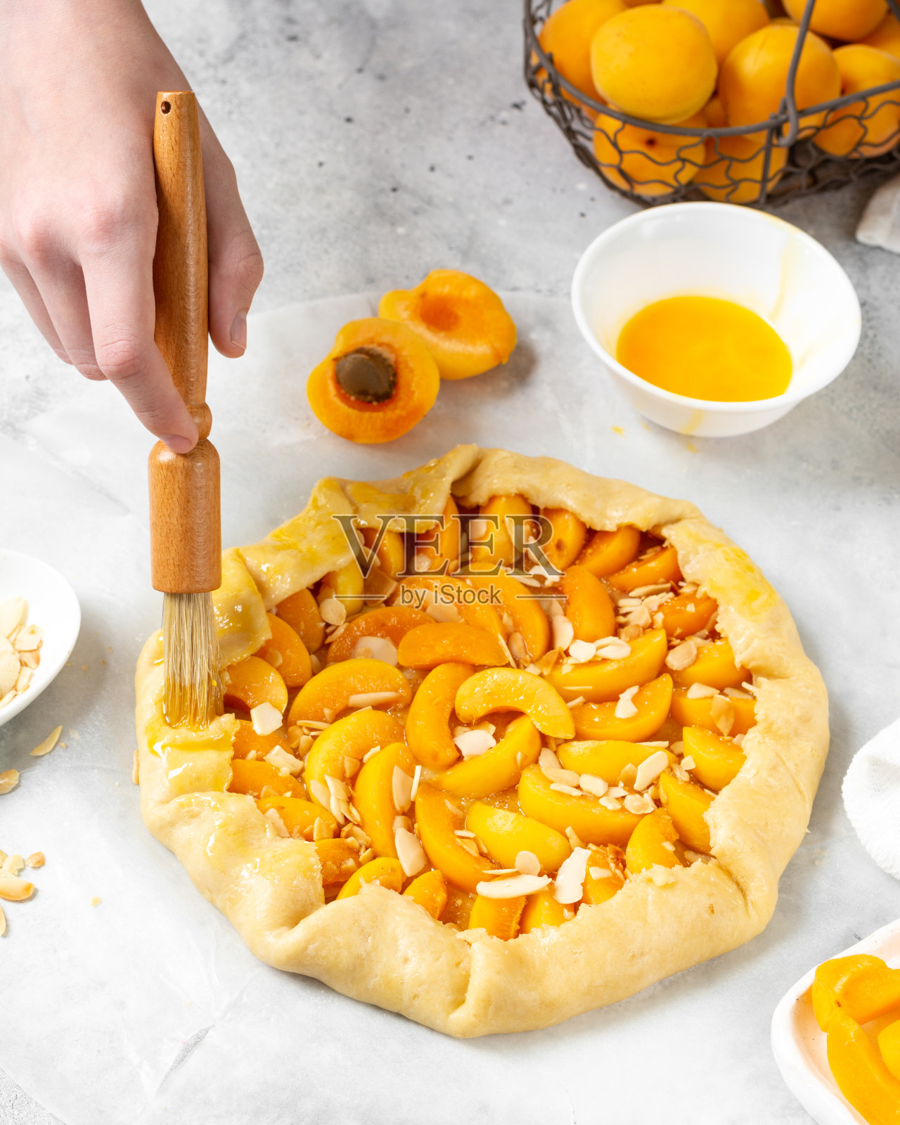 杏仁饼用杏和杏仁做法式酥饼或派的过程夏季烘焙的配料在一个轻的餐桌上的特写。在面团边缘涂上蛋黄。手在框架里照片摄影图片