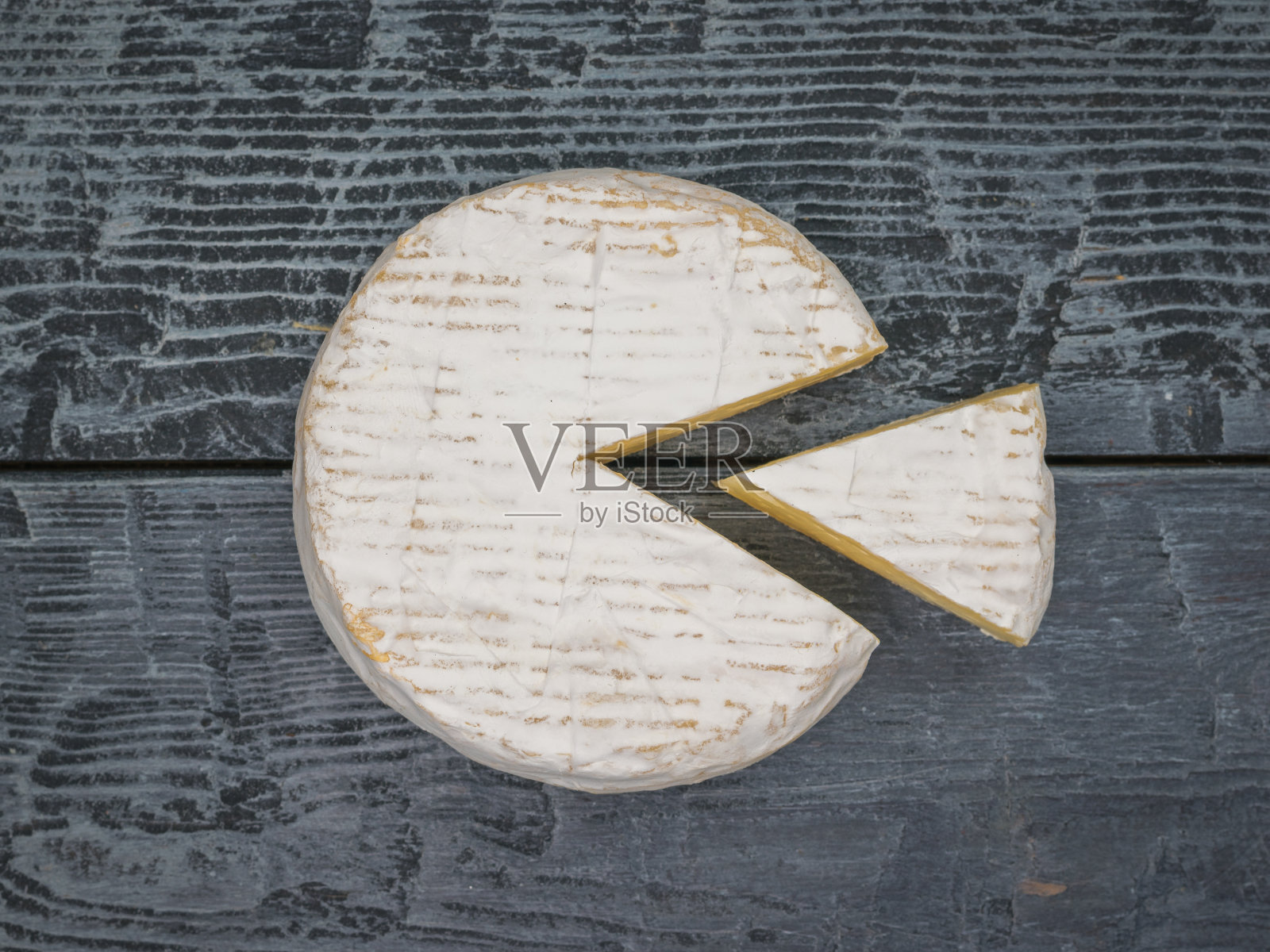 在木桌上放一块切好的卡门贝尔奶酪。照片摄影图片