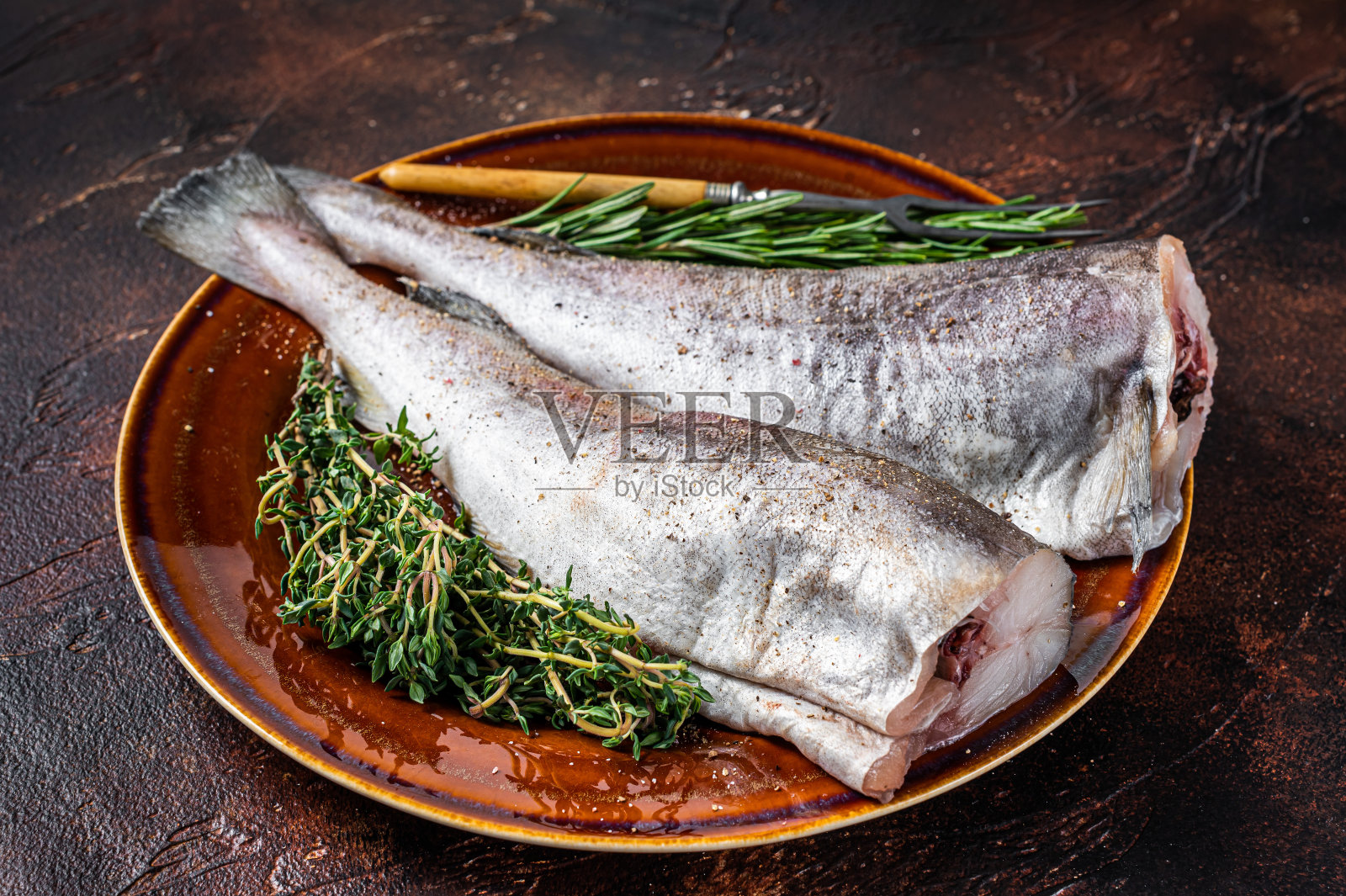 生鳕鱼或鳕鱼，用香草和叉子盛在质朴的盘子里。黑暗的背景。俯视图照片摄影图片