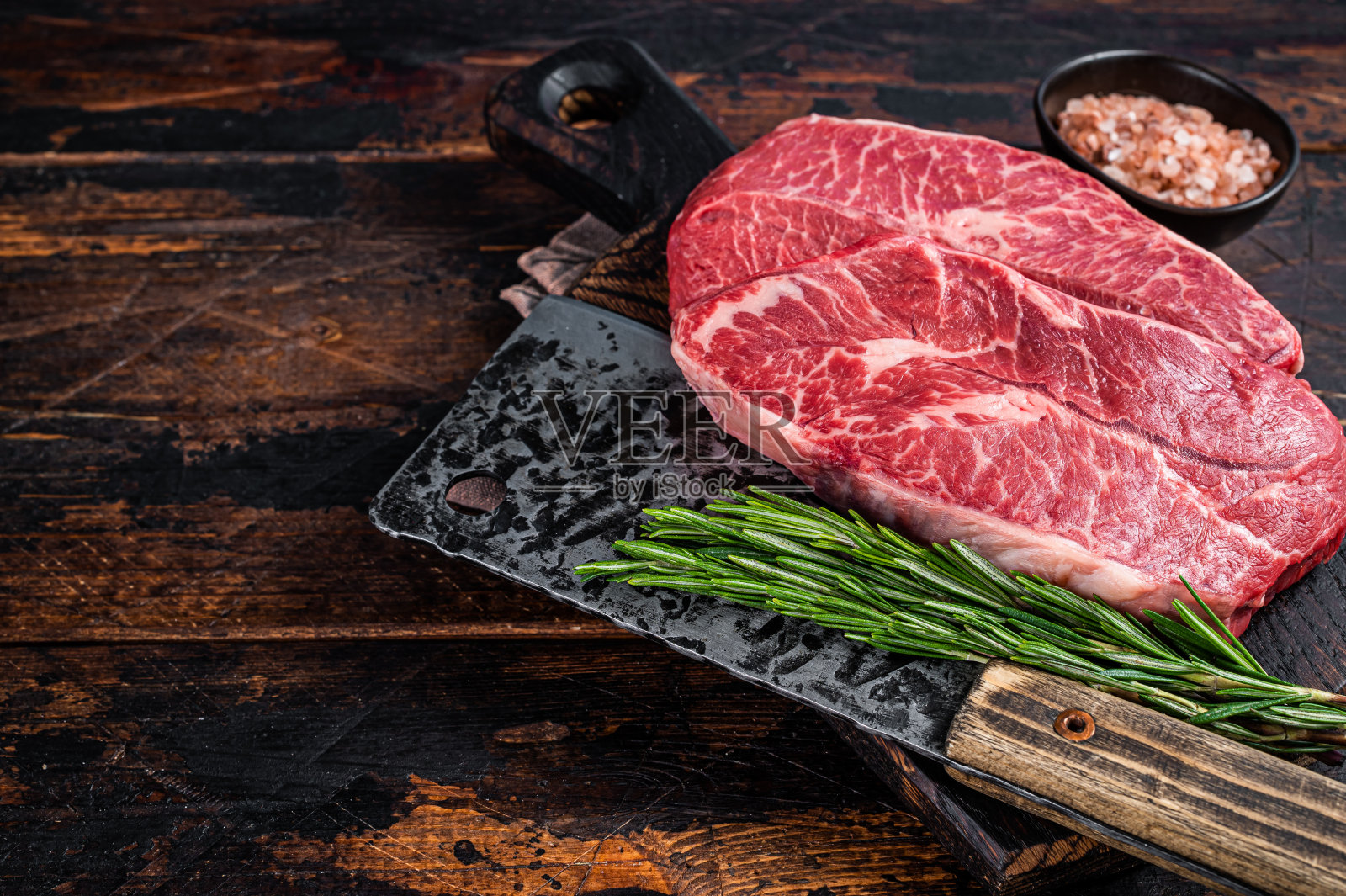 生的生肩片或用切肉刀放在木板上的扁铁牛排。深色木制背景。前视图。本空间照片摄影图片