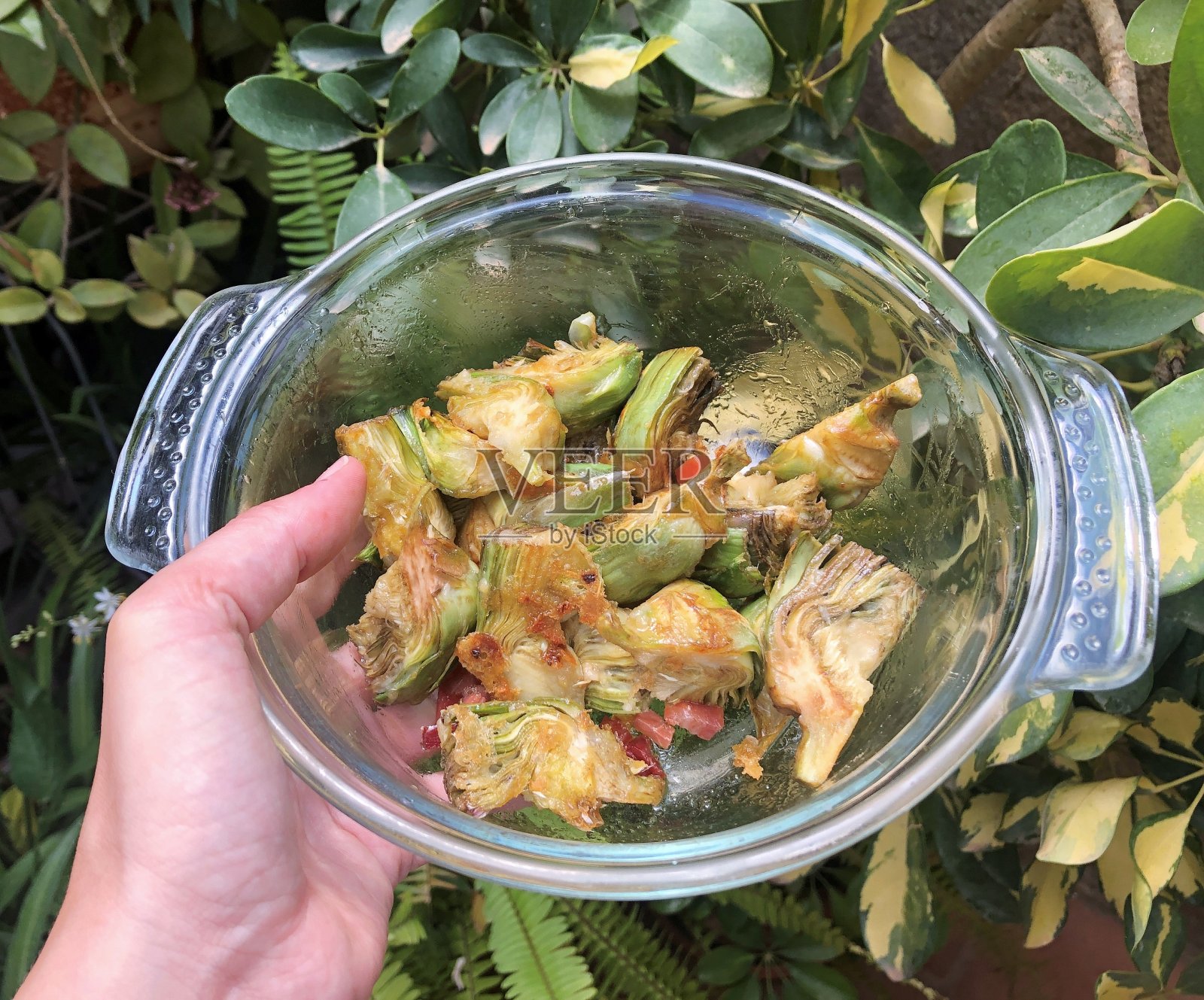 炸洋蓟与火腿一起煮在玻璃碗中，以夏季植物为背景的手食人照片摄影图片