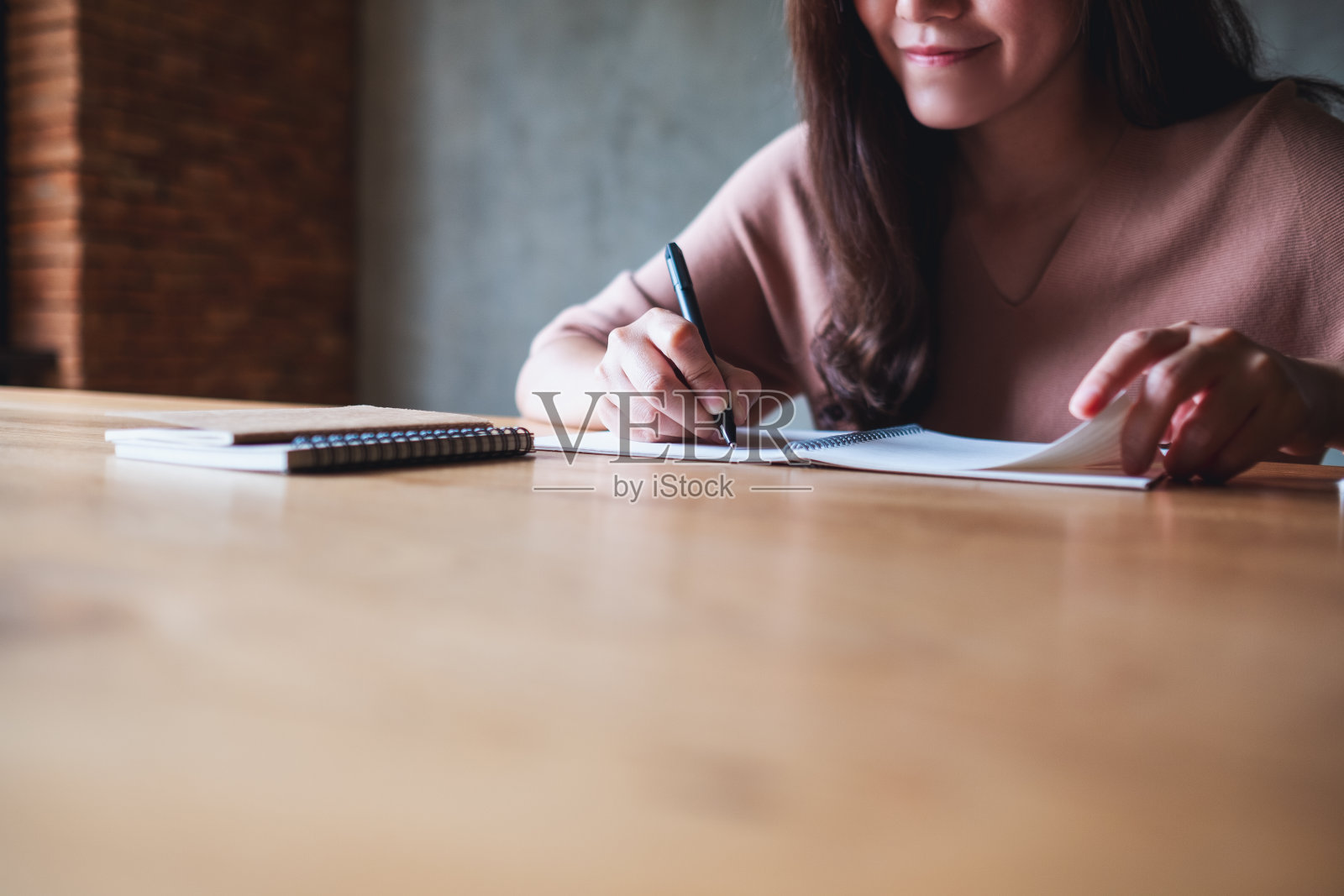 一个漂亮的年轻女子在木桌上的笔记本上写字照片摄影图片