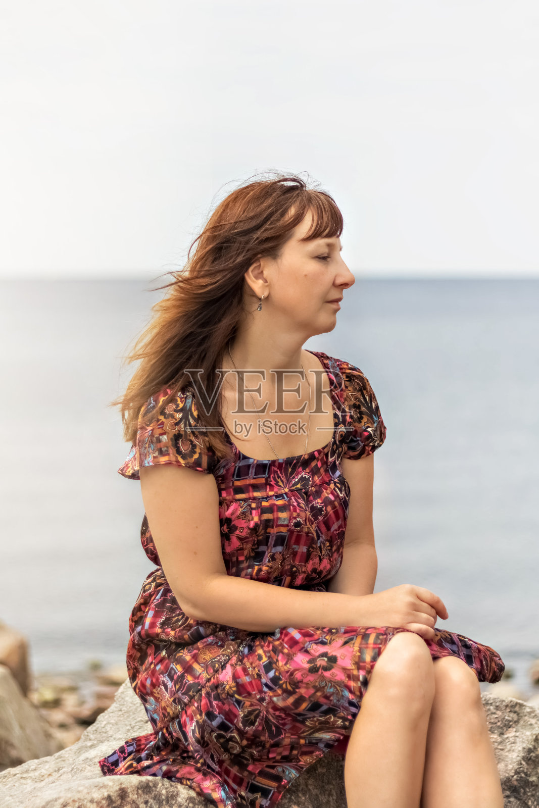 一个穿着夏装的年轻女子正坐在海边的岩石上照片摄影图片