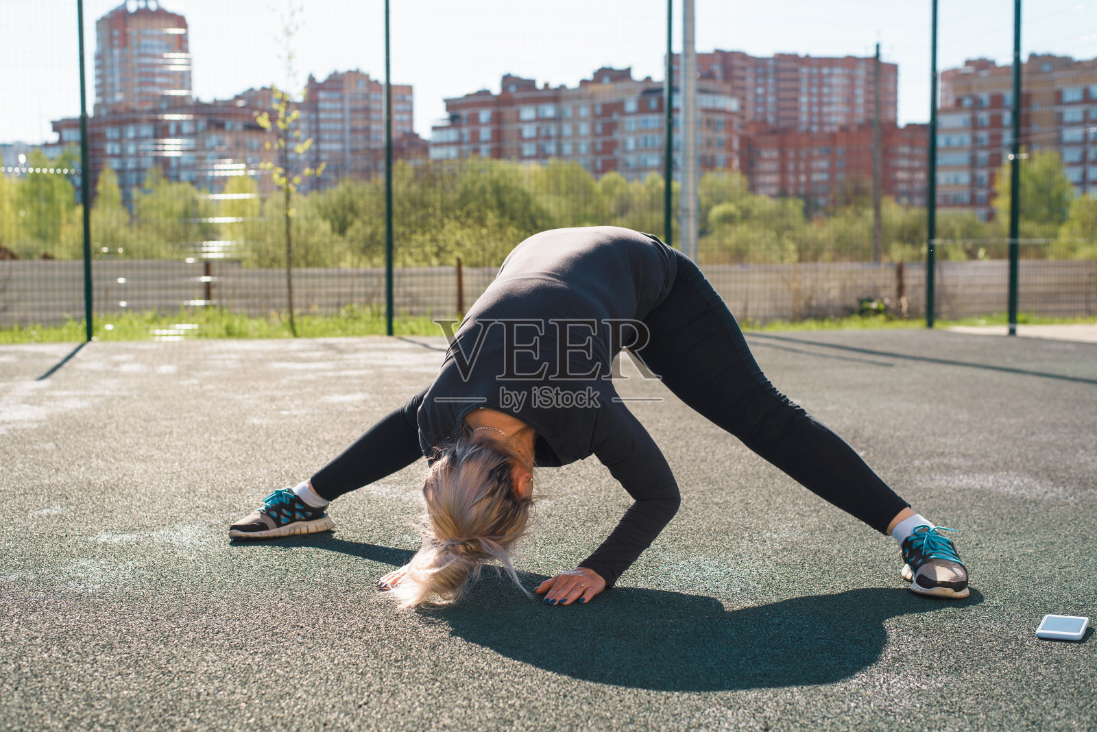 一个夏天的早晨在户外做伸展运动的女人。在操场上训练，在室外。手机旁边的女运动员。灵活性,积极的生活方式。照片摄影图片
