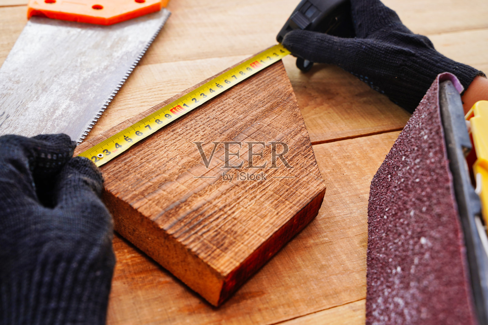 在工作场所测量木板时戴手套的木匠。用木材制作手工制品。照片摄影图片