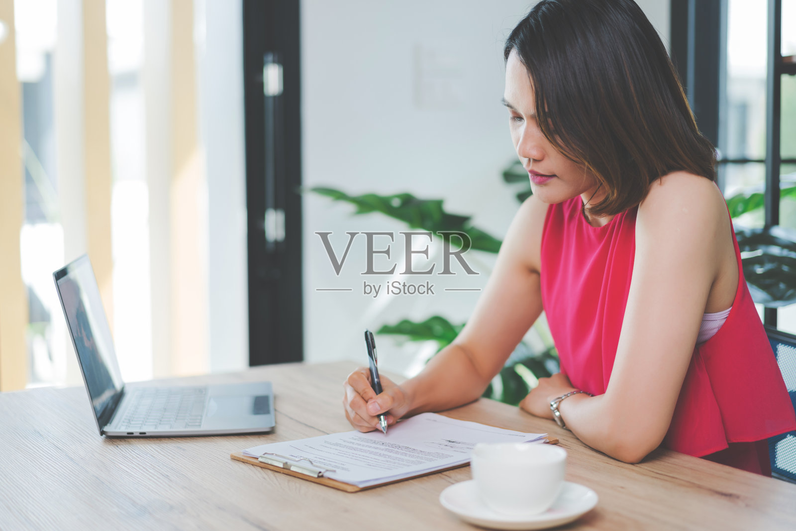 一个快乐的中年亚洲女商人，穿着休闲的服装在家工作，在电脑上检查电子邮件，在财务会计文件纸上写作。库存图片照片摄影图片