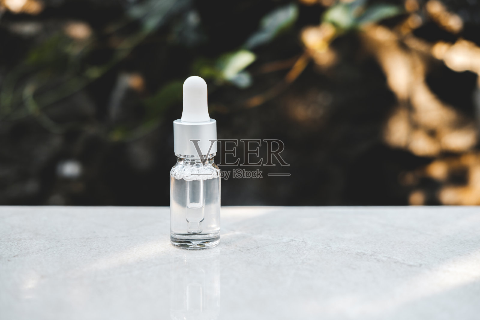 透明色血清瓶在灰色混凝土背景与自然光线。时尚的风格。化妆品模型。Copyspace。照片摄影图片