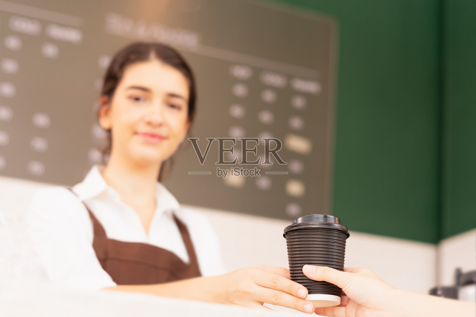 右手边的外卖咖啡杯在顾客和美丽的白人女咖啡师谁看其他地方，专注于咖啡杯照片摄影图片