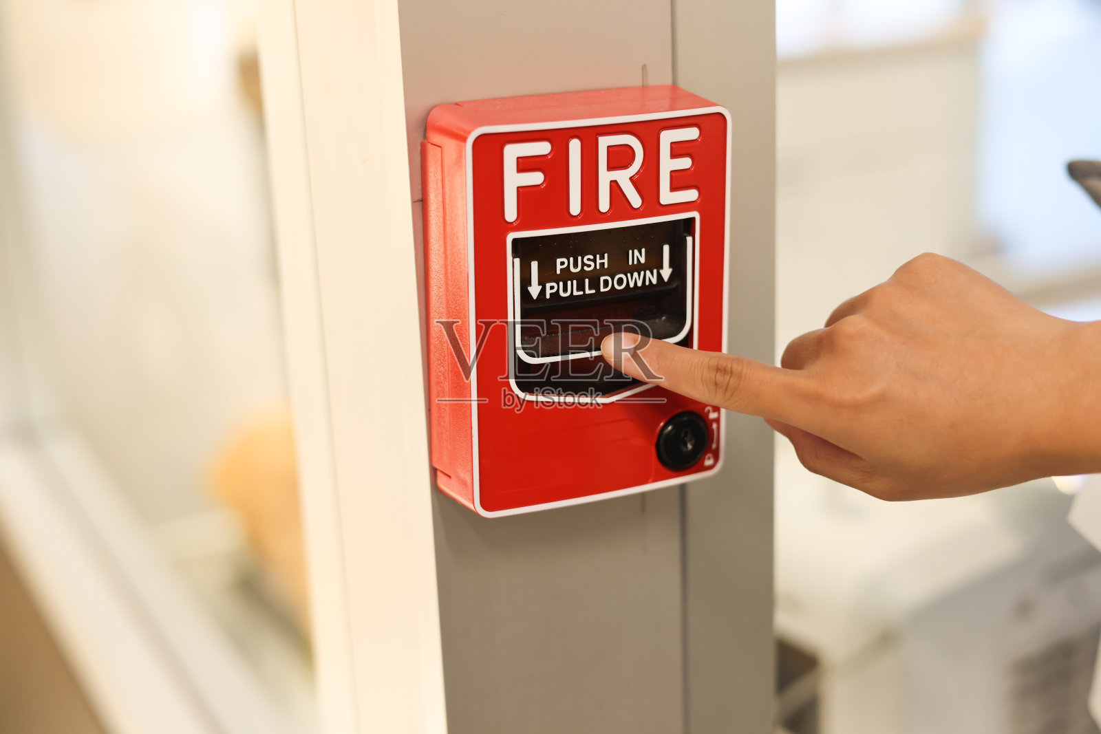 男用手指着办公楼混凝土墙上的红色火警开关。工业火灾报警系统应急设备。照片摄影图片