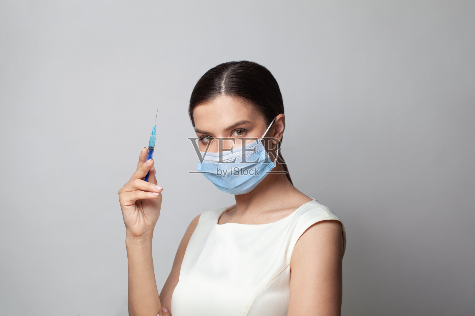 年轻女子在保护医疗面罩与注射器在她的手在白色背景照片摄影图片
