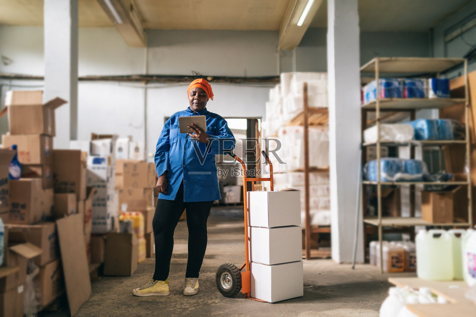 非洲裔女性仓库工人使用一辆手推车，在平板电脑上检查发货情况照片摄影图片
