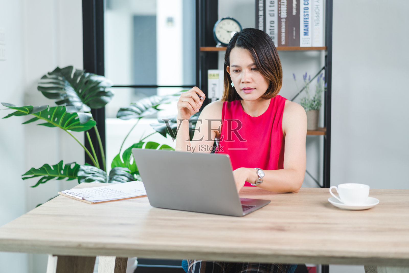 一位快乐的中年亚洲女商人，穿着休闲的休闲装在家工作，在电脑上查看电子邮件，在财务会计凭证上写作。商业库存图片照片摄影图片