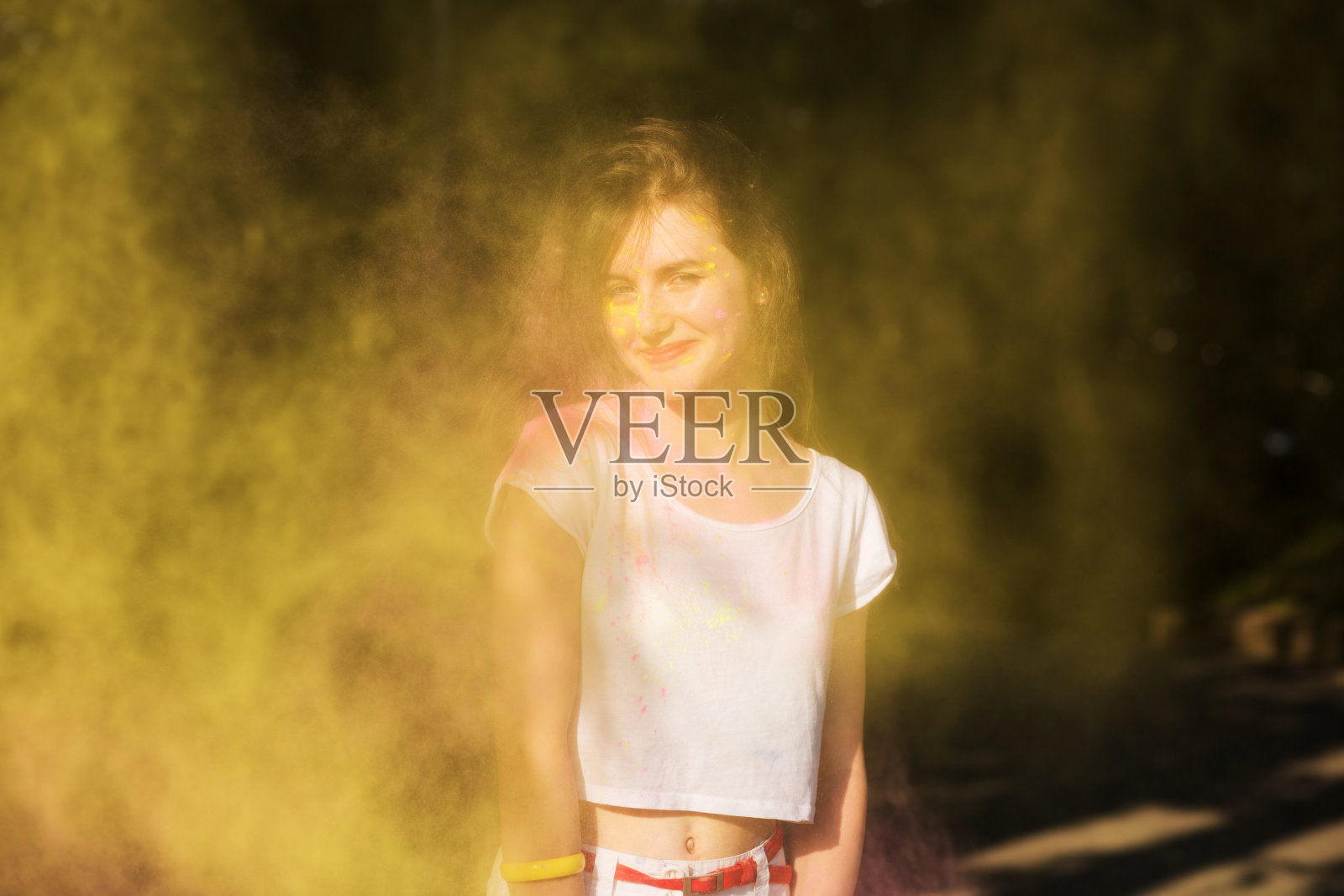 在胡里节上，微笑的黑发模特在一团黄色的干油漆中玩得很开心照片摄影图片