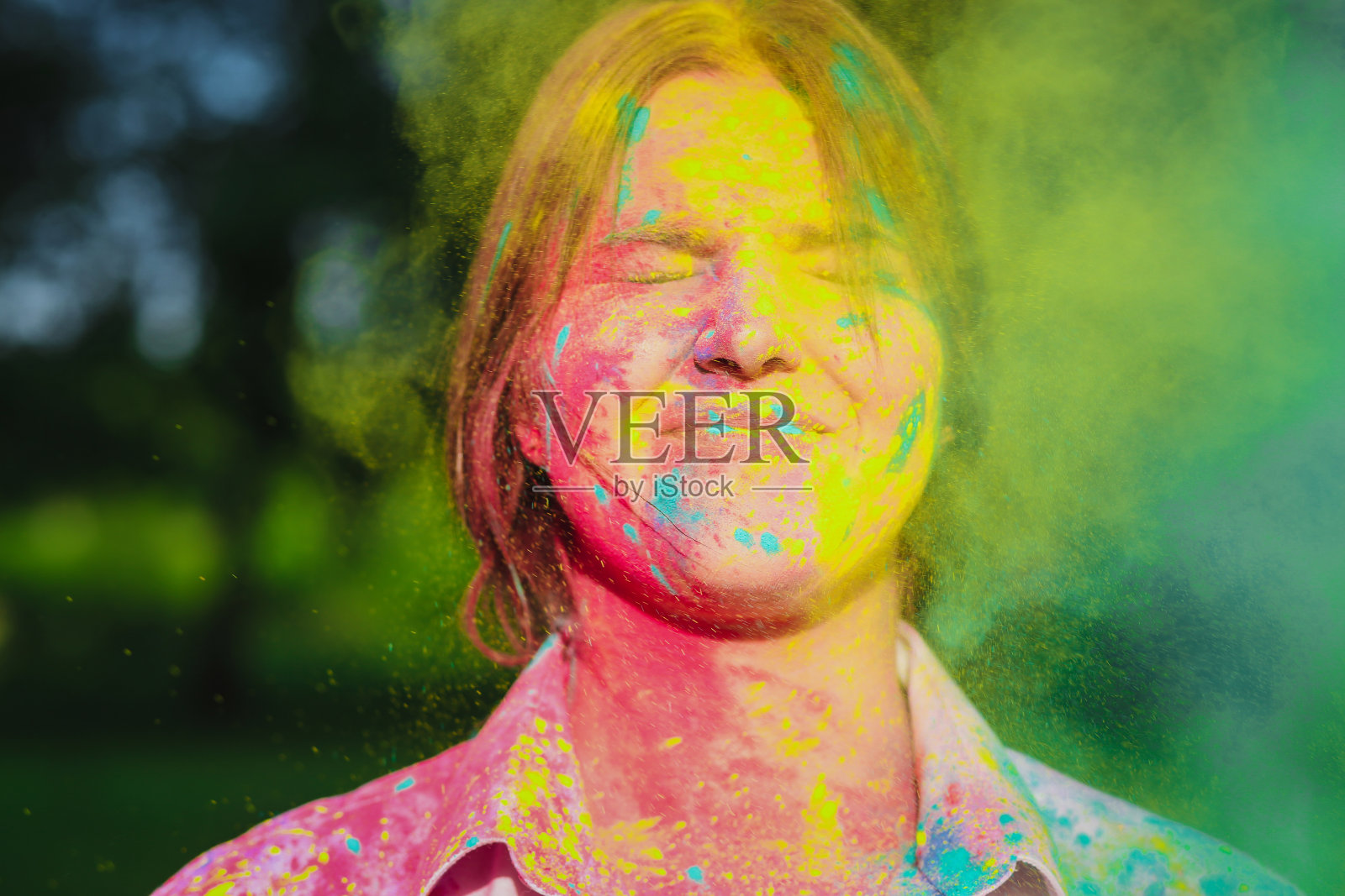 令人惊叹的黑发短发模特在公园里用黄色和绿色的胡里颜料摆姿势。空的空间照片摄影图片