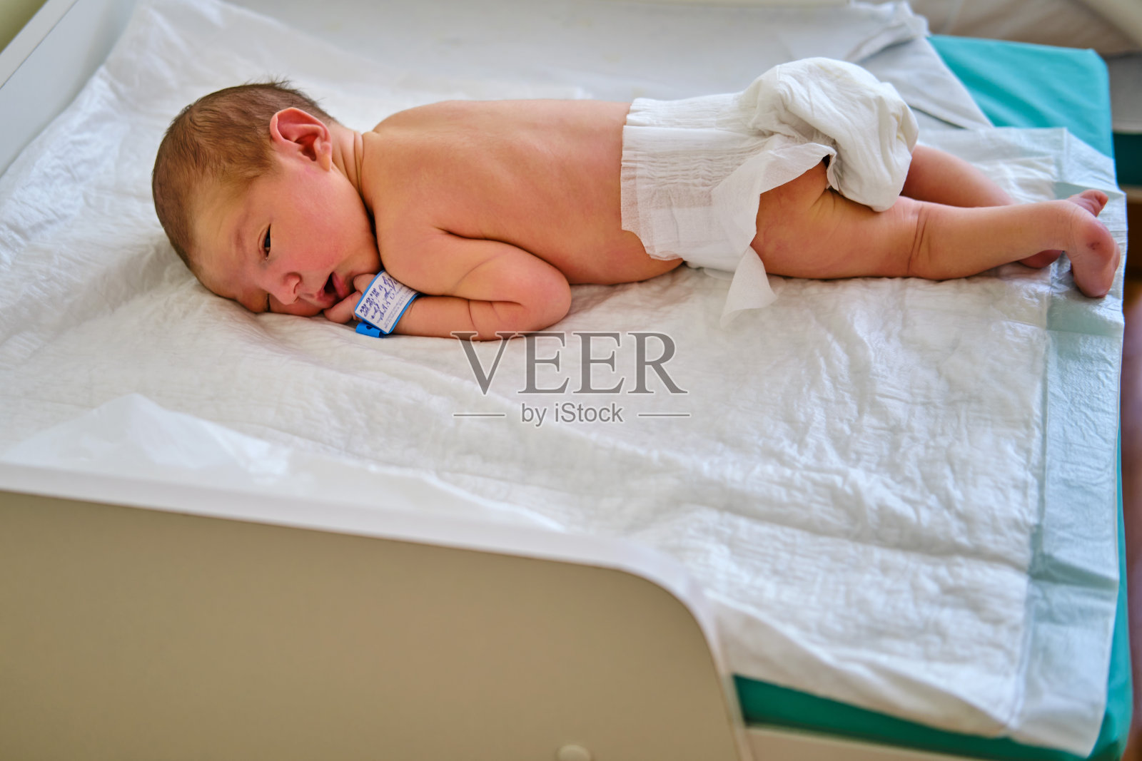 一个刚出生的婴儿手臂上戴着产科医院的手镯，放在换尿布的桌子上照片摄影图片