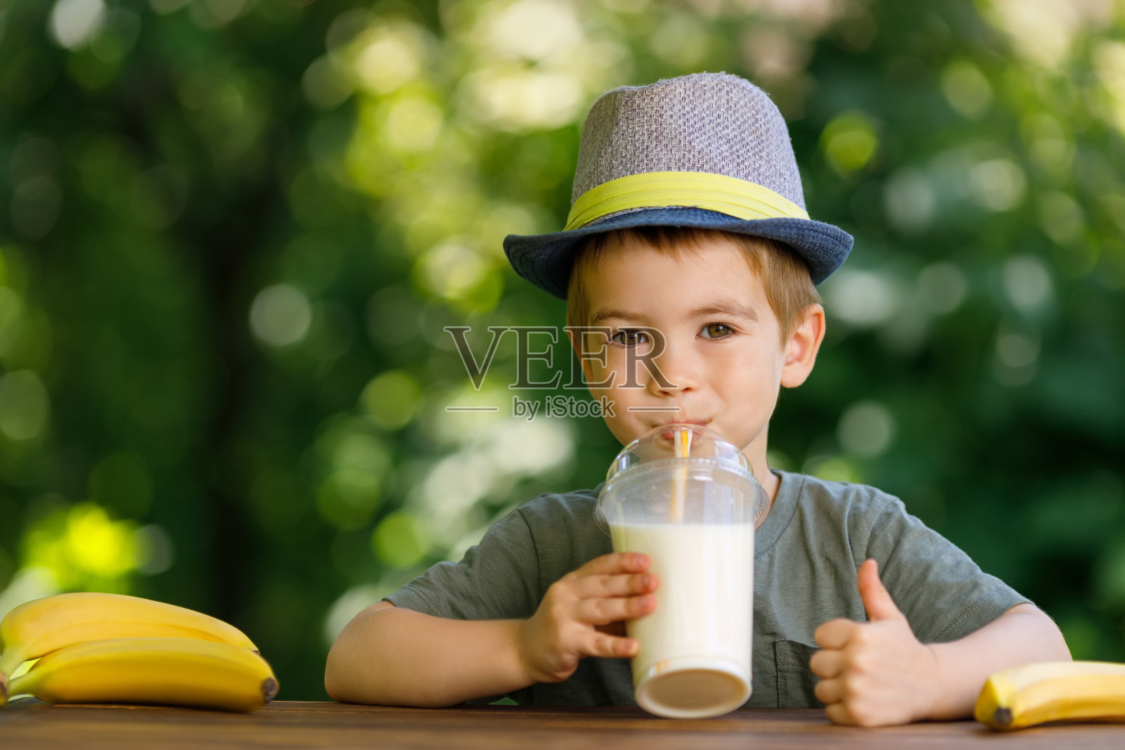 小男孩用一次性塑料玻璃杯喝香蕉奶昔照片摄影图片