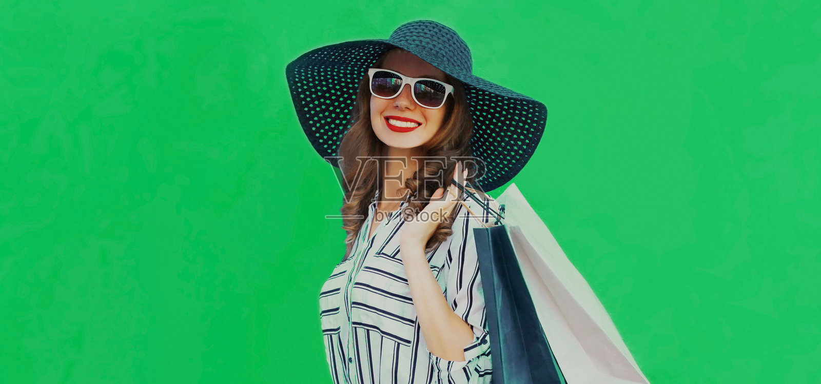 漂亮的年轻女人的肖像购物袋戴着黑色圆形的夏帽，白色条纹衬衫在绿色的背景照片摄影图片