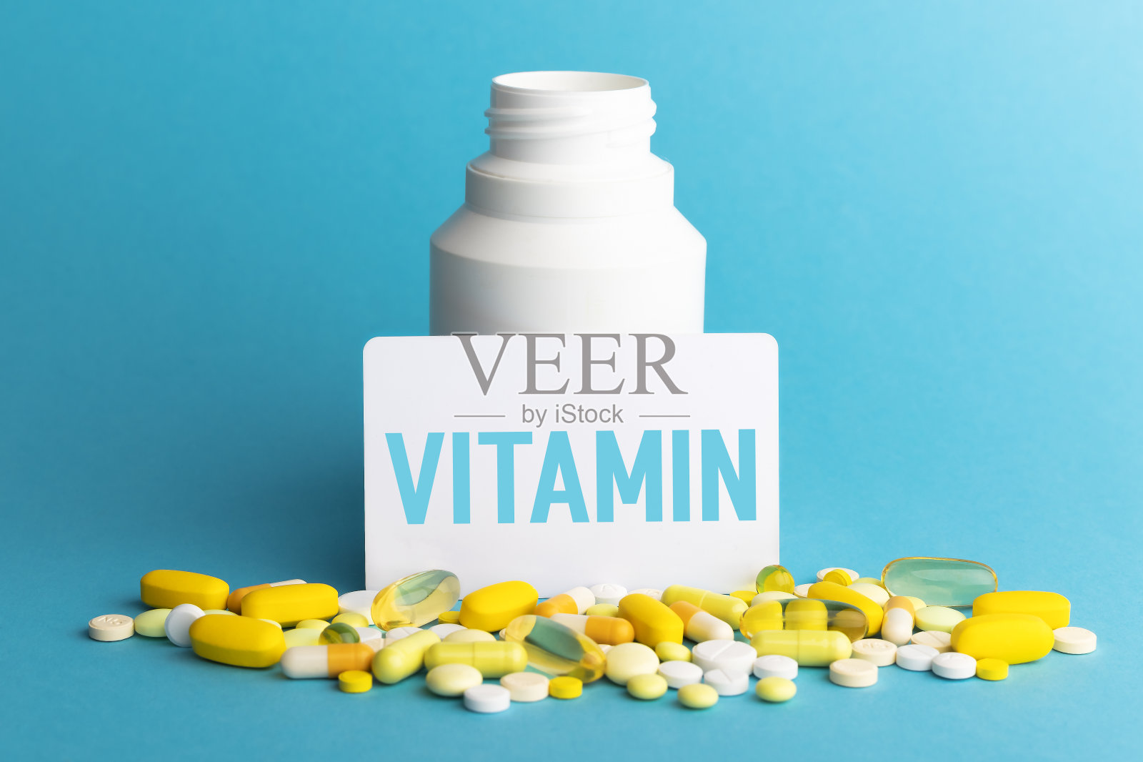 在卡片上写上维生素。瓶子里有蓝色背景的彩色药丸。医学概念。特写镜头。照片摄影图片