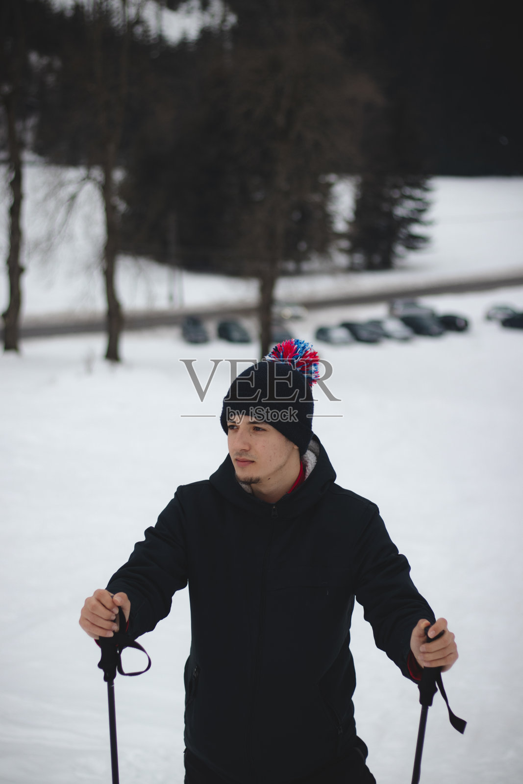 一个十几岁的男子在捷克共和国东部的贝斯基迪山谷观看滑雪坡上发生的事情的特写。冬天。戴着帽子，拿着绒球的男人。教练看着他的收费照片摄影图片