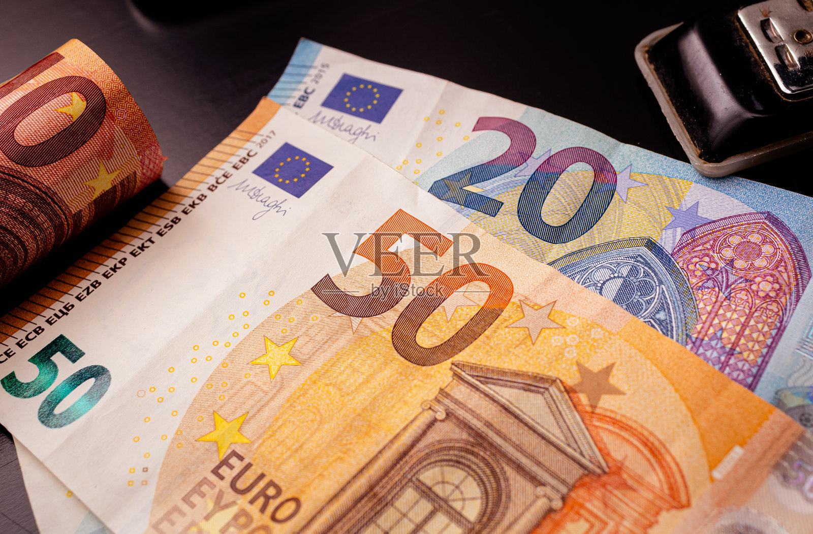 货币，欧元。深色的桌子上放着欧元钞票。50欧元纸币的亮点。排版用的黑色订书机照片摄影图片