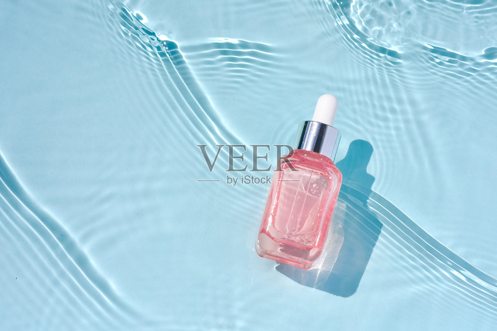 医用美容护肤，带胶原蛋白的粉红色玻璃血清瓶，碧水背景，波浪照片摄影图片
