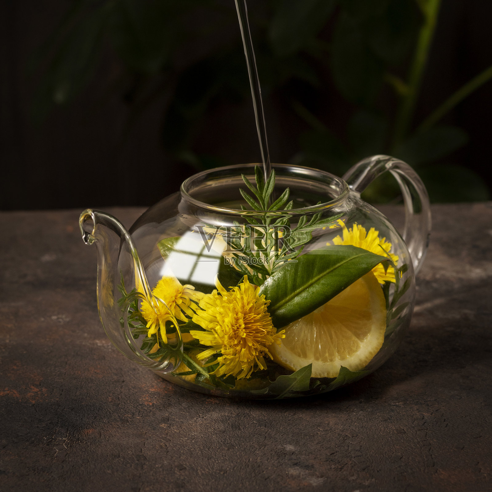 茶在玻璃茶壶与香草，鲜花和柠檬片在黑暗的背景照片摄影图片