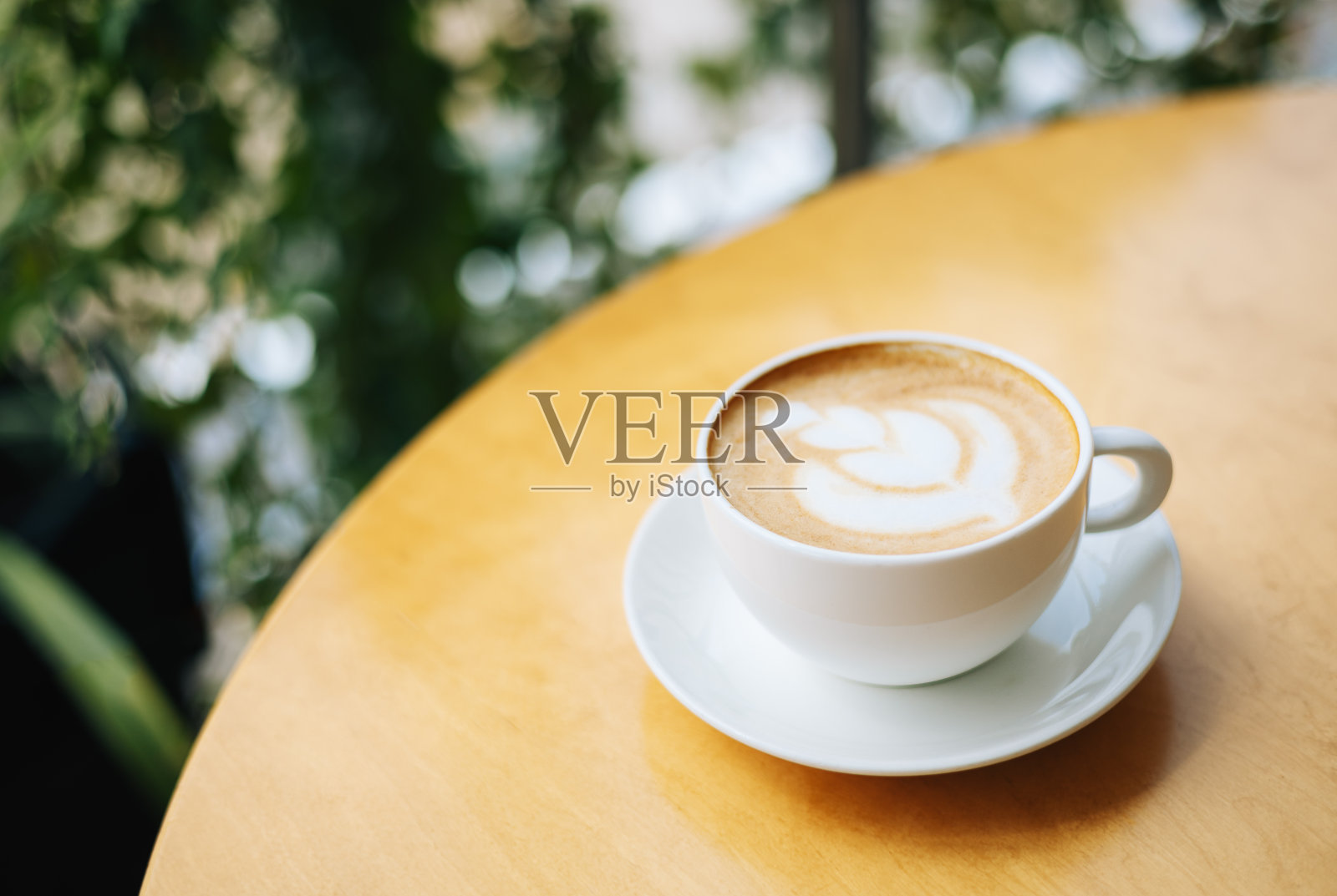 在咖啡馆的木桌上，一杯带有拿铁艺术的咖啡。照片摄影图片