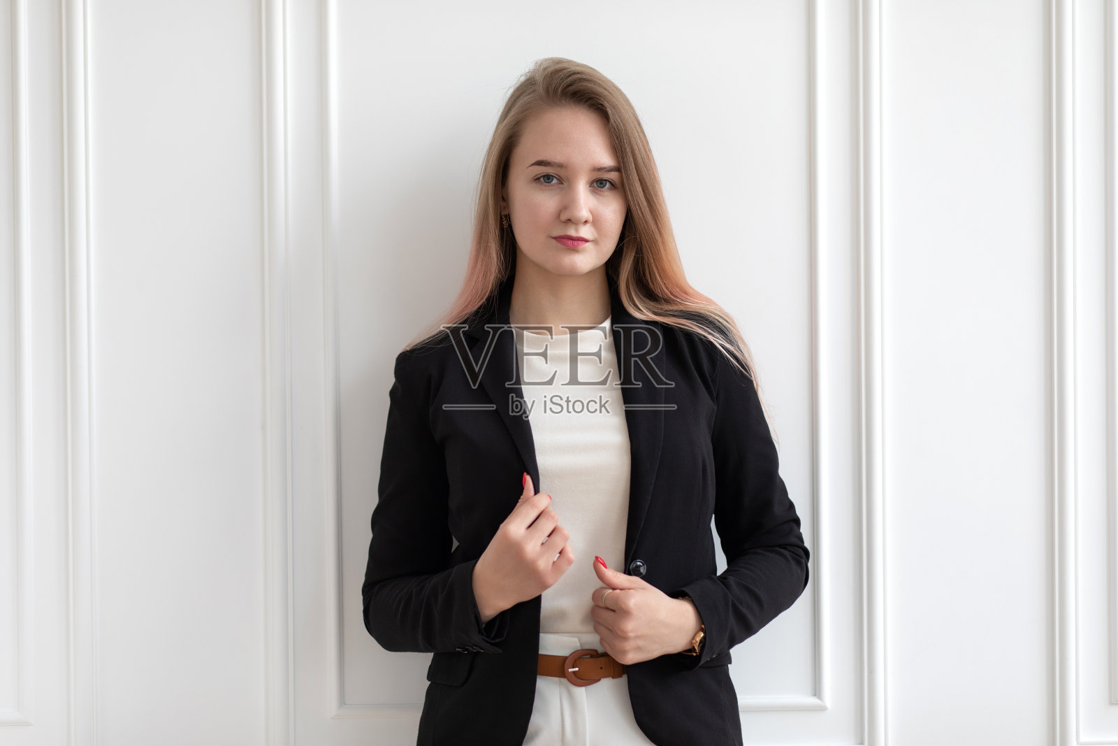 年轻美丽的白种女人在休闲办公室衣服站着，拿着黑色夹克，摆姿势。照片摄影图片