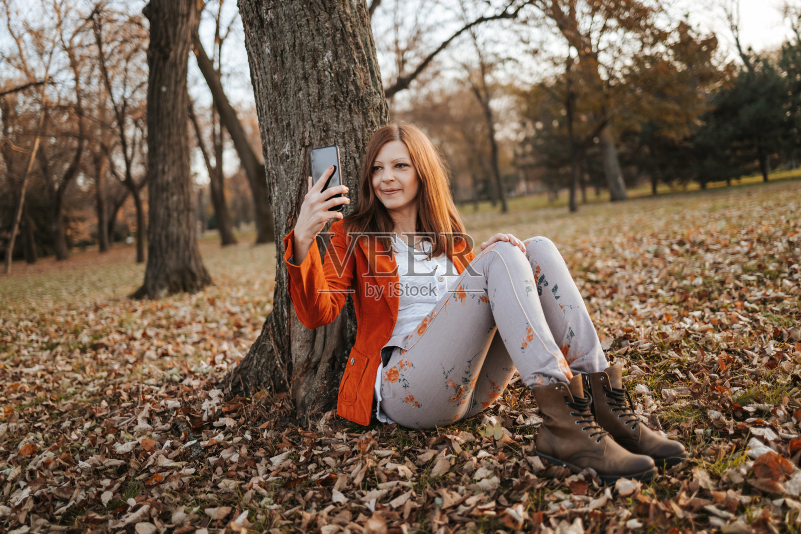 美丽的年轻女子在秋天的时候坐在公园的树下自拍照片摄影图片
