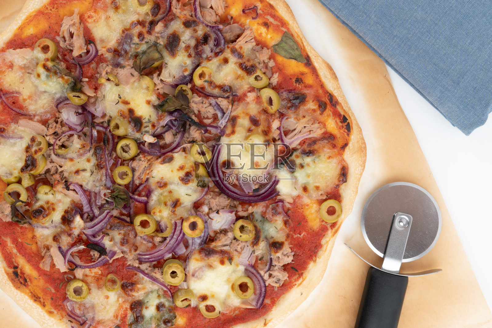 俯视图工作室拍摄的新鲜烤披萨在烤纸上，孤立的白色背景。蓝布和披萨切片机。照片摄影图片